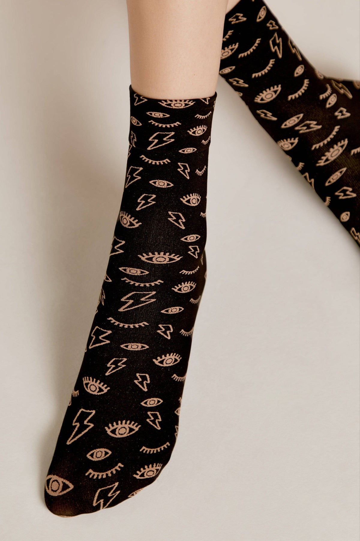 A pair of crew socks in black featuring a repeating pattern of light beige lightning bolts and stylized open eyes.