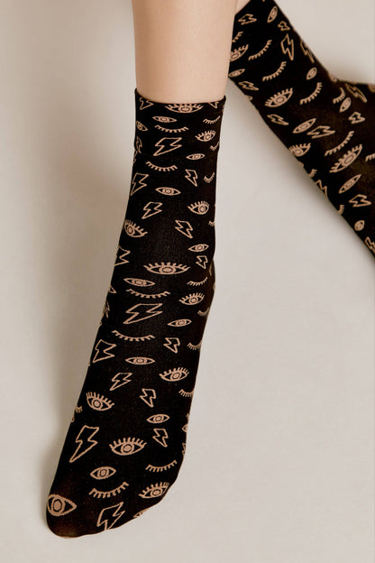 A pair of crew socks in black featuring a repeating pattern of light beige lightning bolts and stylized open eyes.