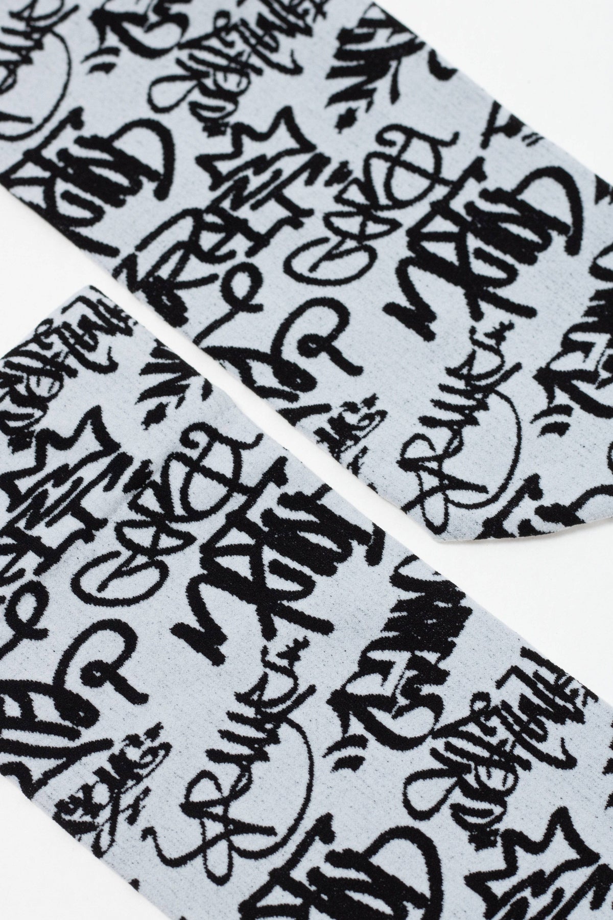 Two pieces of light blue fabric decorated with an all-over black graffiti-style pattern of overlapping hand-drawn letters and symbols.