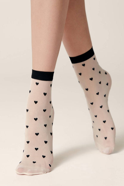 Sheer ankle socks in a light beige tone, featuring an all-over pattern of small black hearts and finished with a solid black trim at the cuffs.