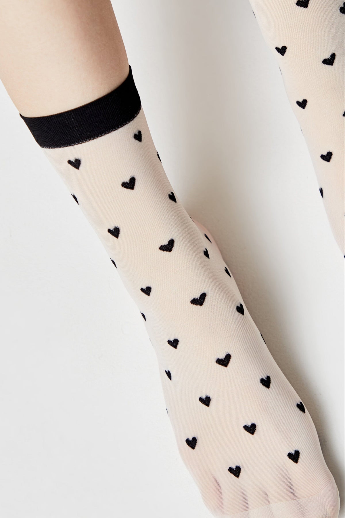 Sheer beige ankle socks decorated with a pattern of small black hearts and finished with a solid black trim at the top.