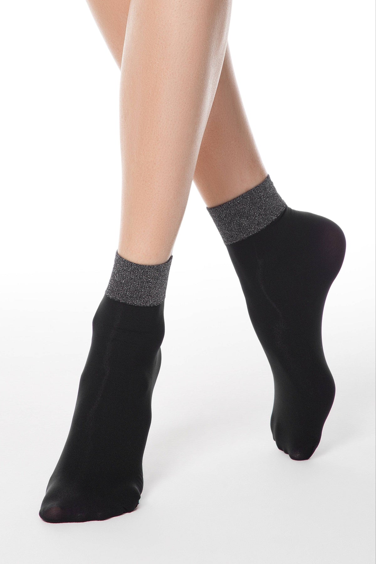 Black ankle socks with a shimmering grey metallic cuff are worn on a pair of legs against a white background.