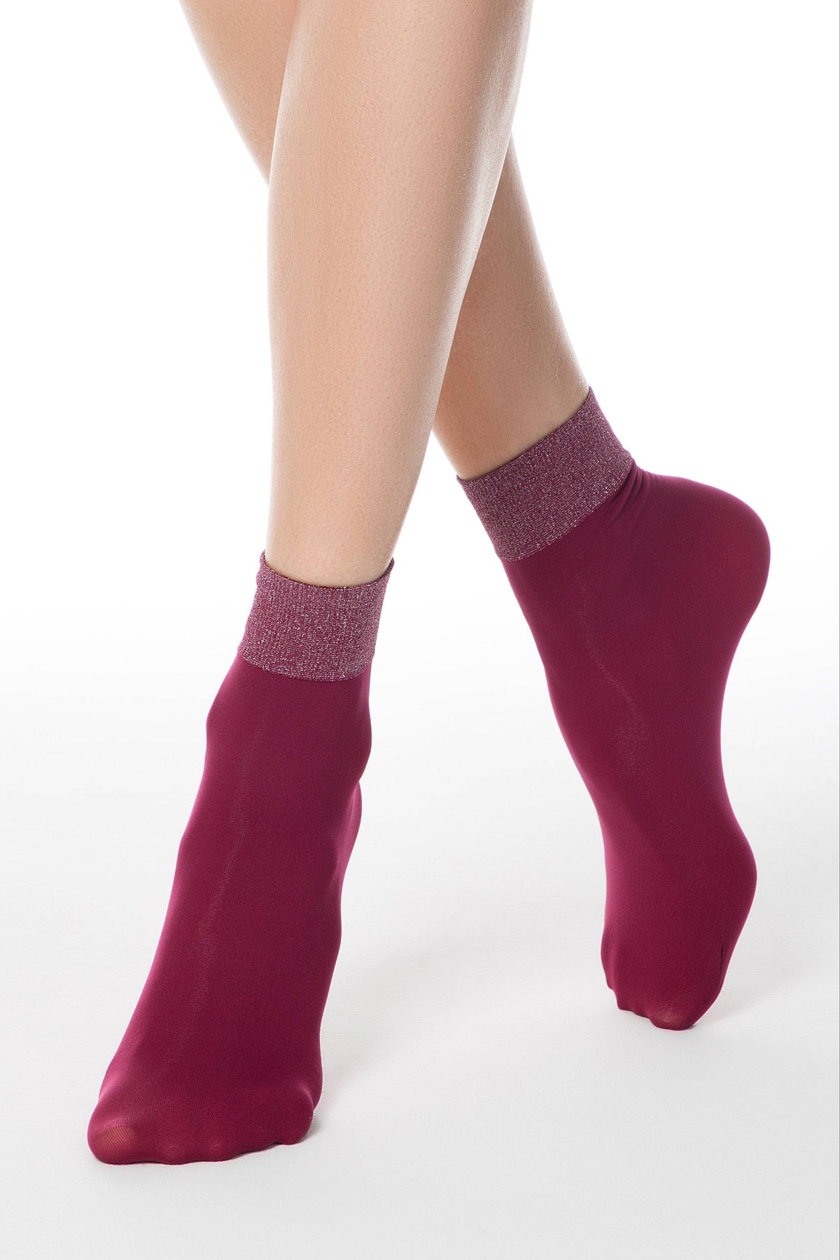A pair of sheer burgundy ankle socks with shimmering glittery cuffs worn on the feet of a person against a white background.