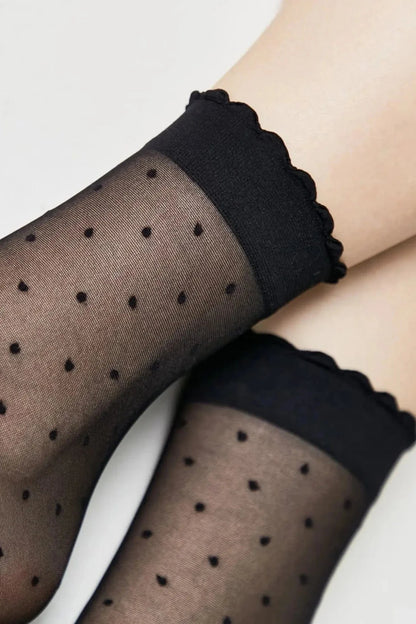 Sheer black ankle socks featuring a black polka dot pattern and a scalloped ruffled edge at the cuff.