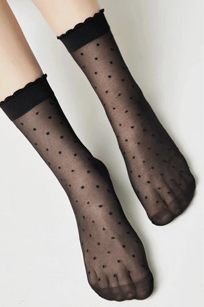 Sheer black ankle socks featuring a subtle polka dot pattern and ruffled trim at the cuffs, modeled on a pair of legs.