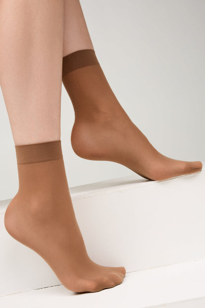 A pair of sheer tan ankle-length hosiery socks worn on a person's feet against a plain white background.