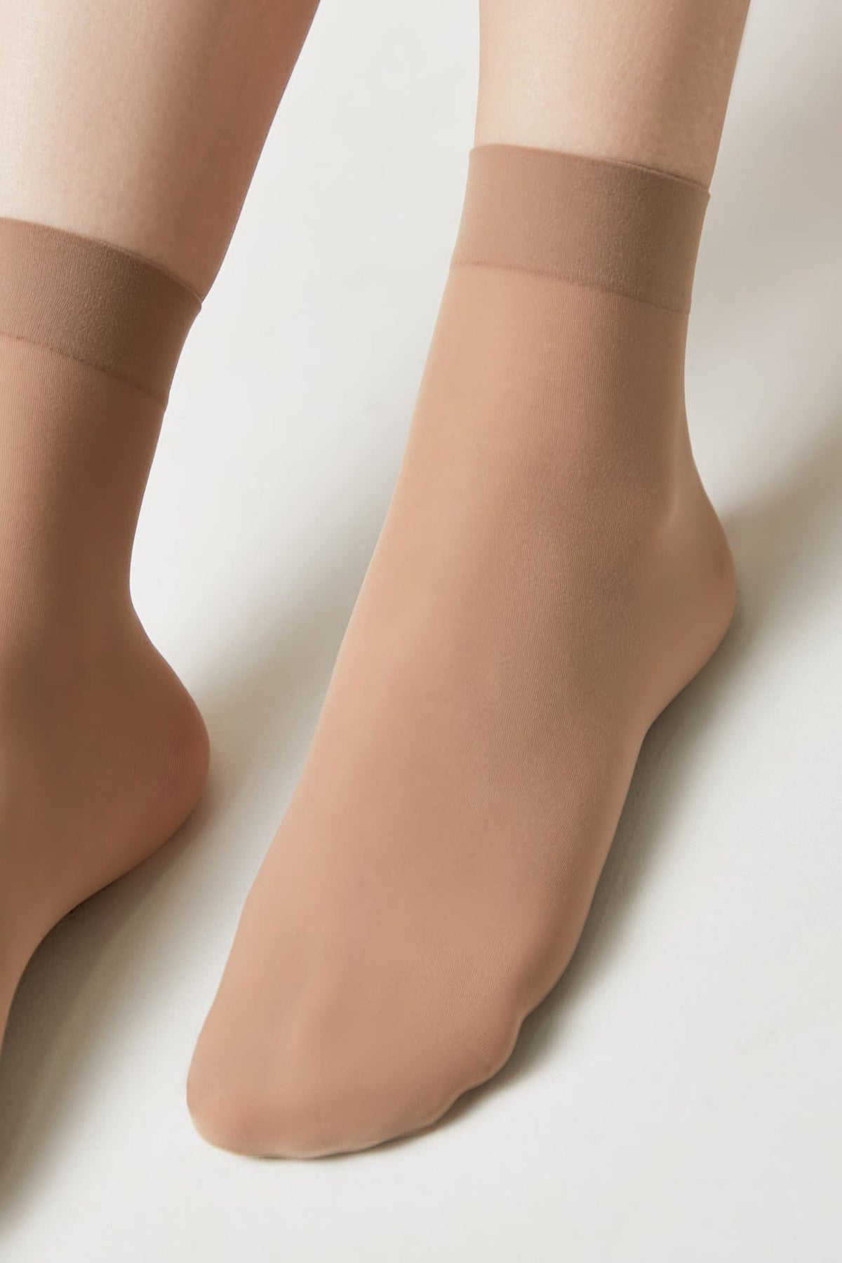 Nude-colored ankle-length sheer hosiery socks worn on feet against a plain light background.
