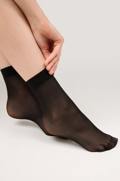Sheer black ankle-high socks worn on a person's feet against a plain light gray background.