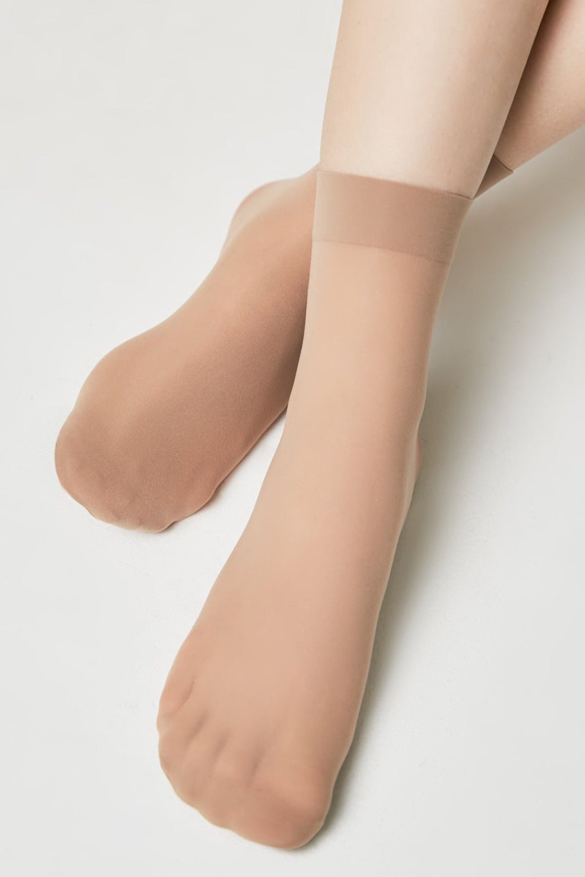 Nude-colored ankle-high hosiery socks worn on a person's feet against a plain white background.