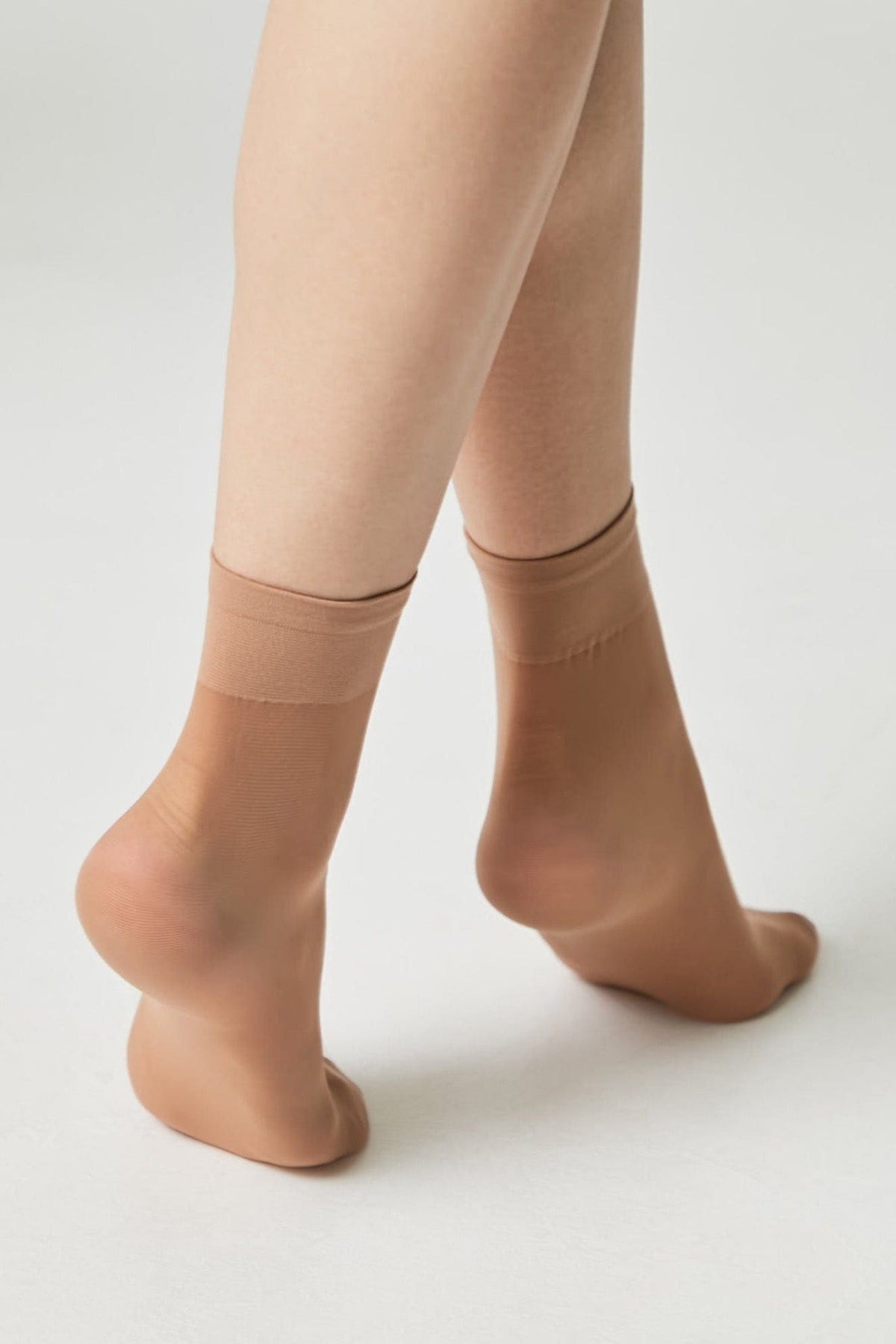 A pair of sheer beige ankle-high socks modeled on a person's feet against a plain white background.