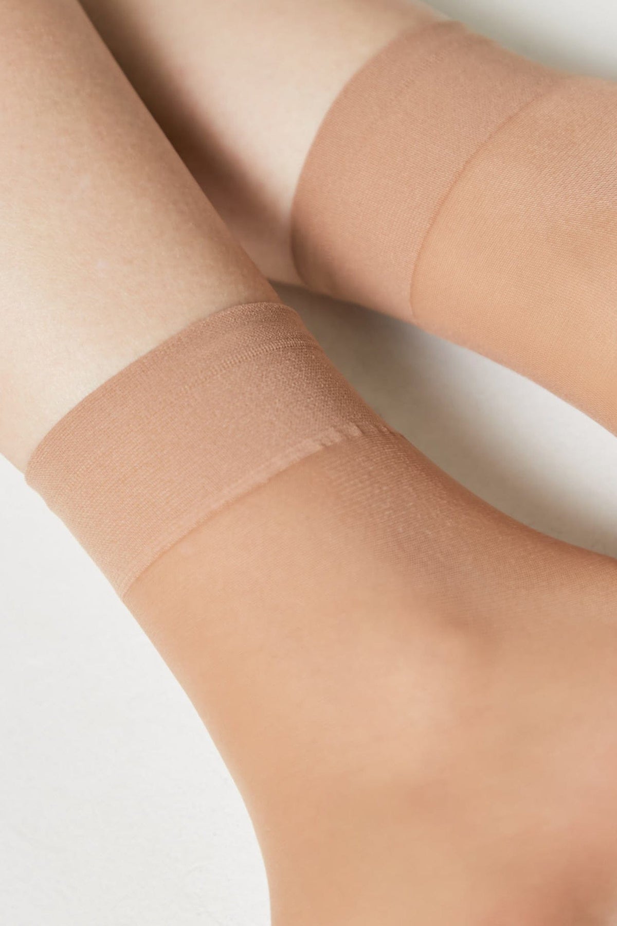 A pair of sheer, nude-colored ankle socks worn on feet against a plain white background.