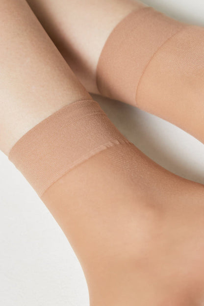 A pair of sheer, nude-colored ankle socks worn on feet against a plain white background.