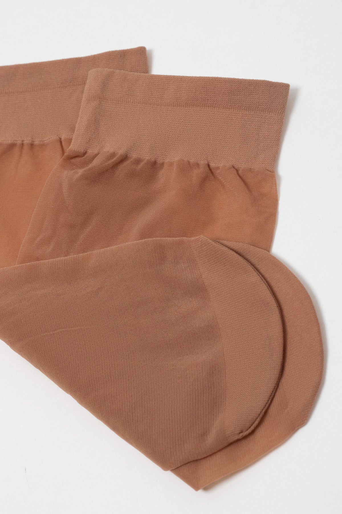 A pair of sheer, tan ankle-high stockings folded over on a plain white surface.