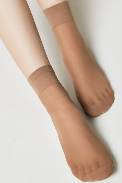 A pair of sheer tan ankle-length hosiery socks worn on a pair of legs against a plain white background.