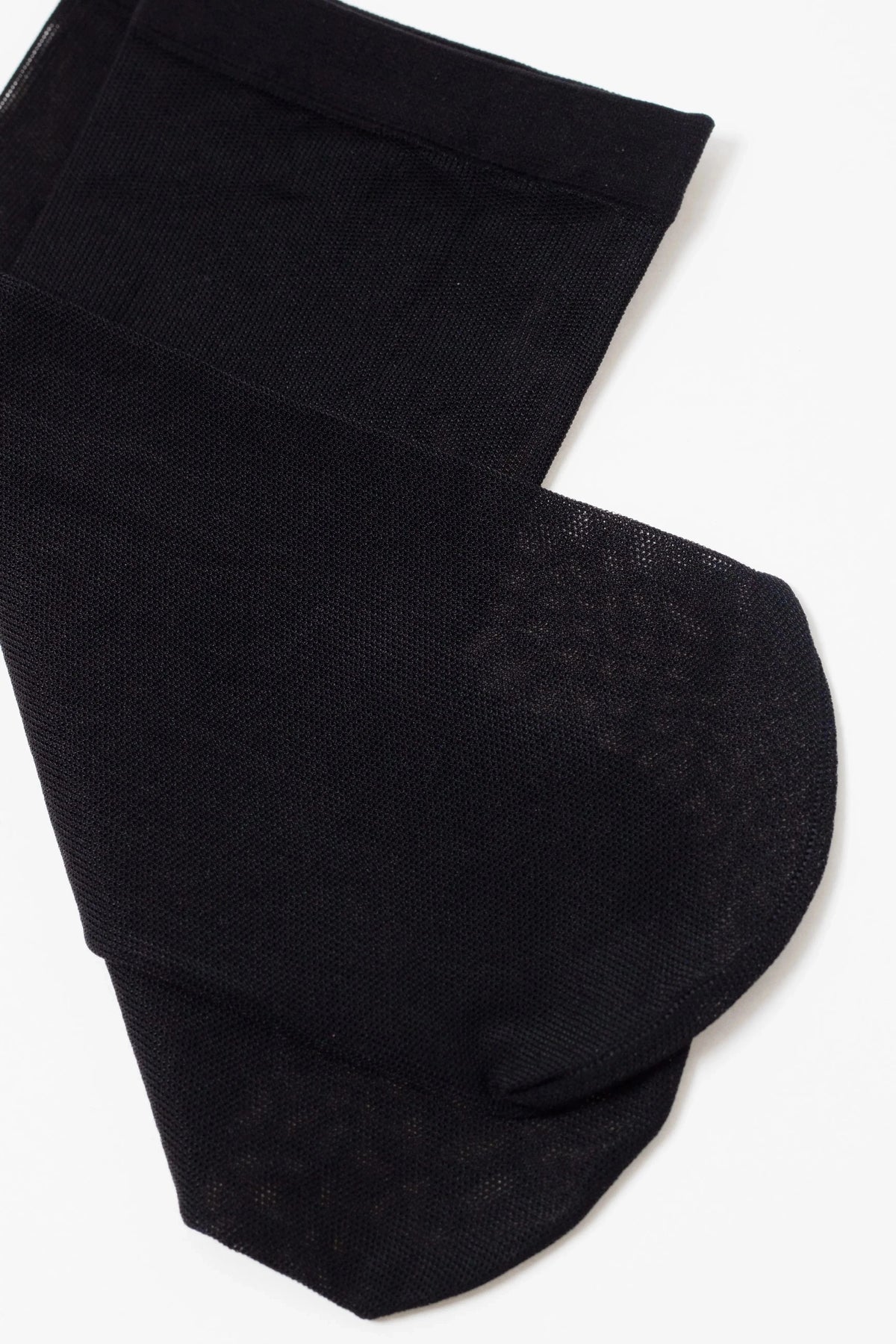 A pair of sheer black stockings laid flat against a white background, showing the reinforced toe and the textured mesh fabric.