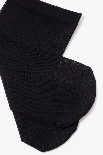 A pair of sheer black stockings laid flat against a white background, showing the reinforced toe and the textured mesh fabric.