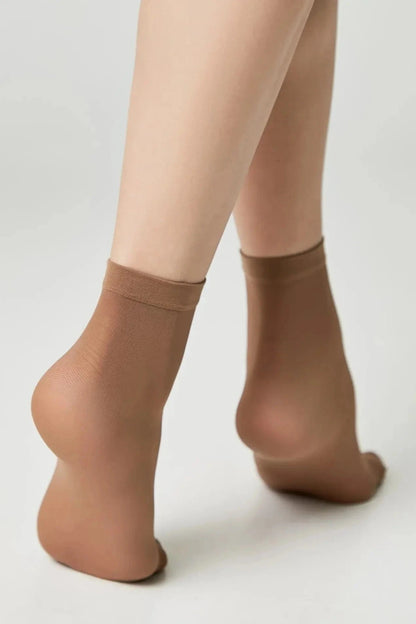Sheer tan ankle socks worn on the feet of a person against a plain white background.