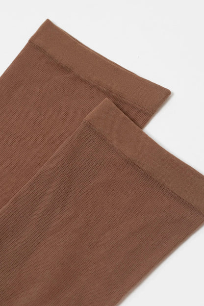 A pair of sheer, brown knee-high stockings are laid against a plain white background, showing the fine mesh texture and the reinforced elastic hem at the top.