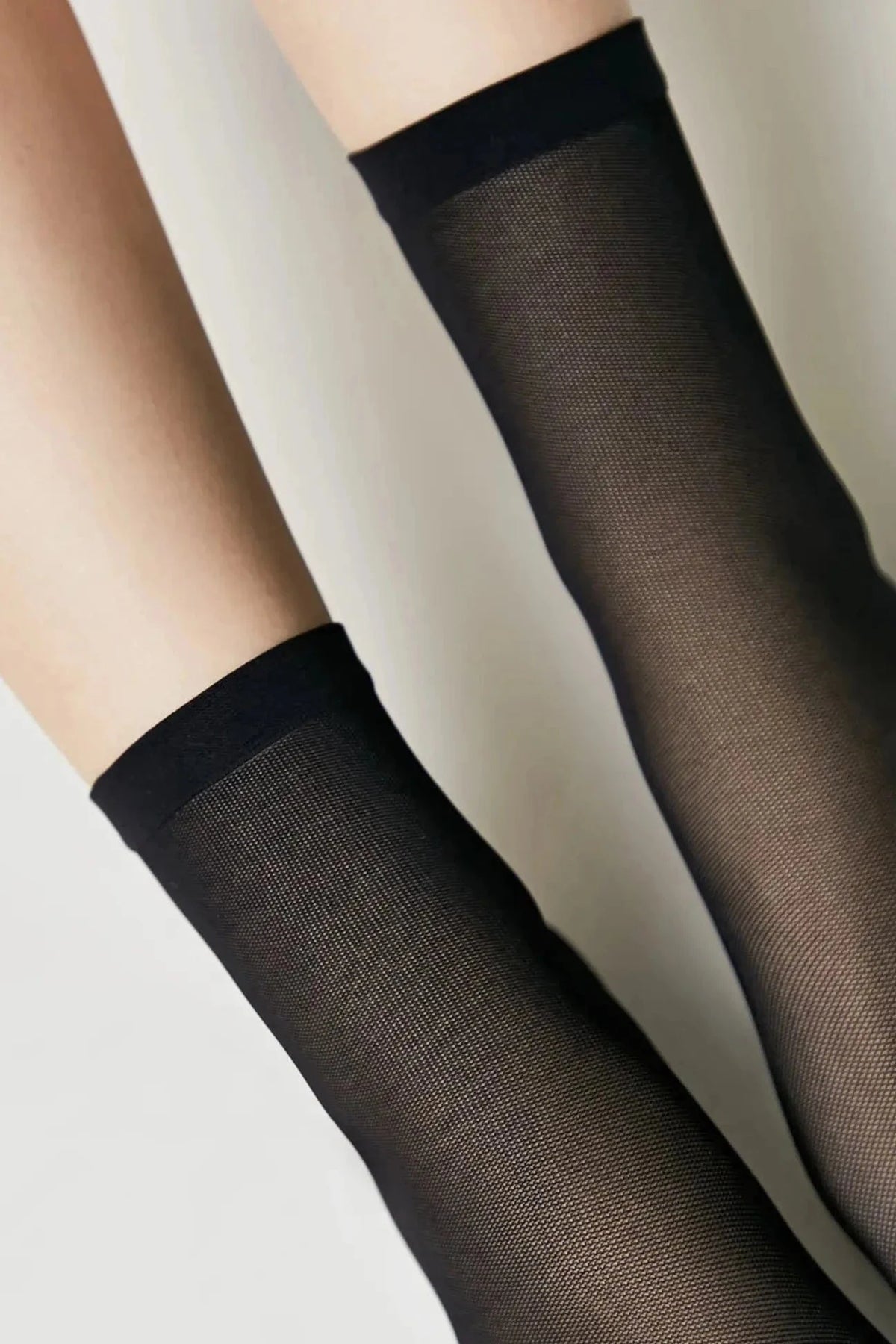A pair of sheer black stockings shown on legs against a plain background.