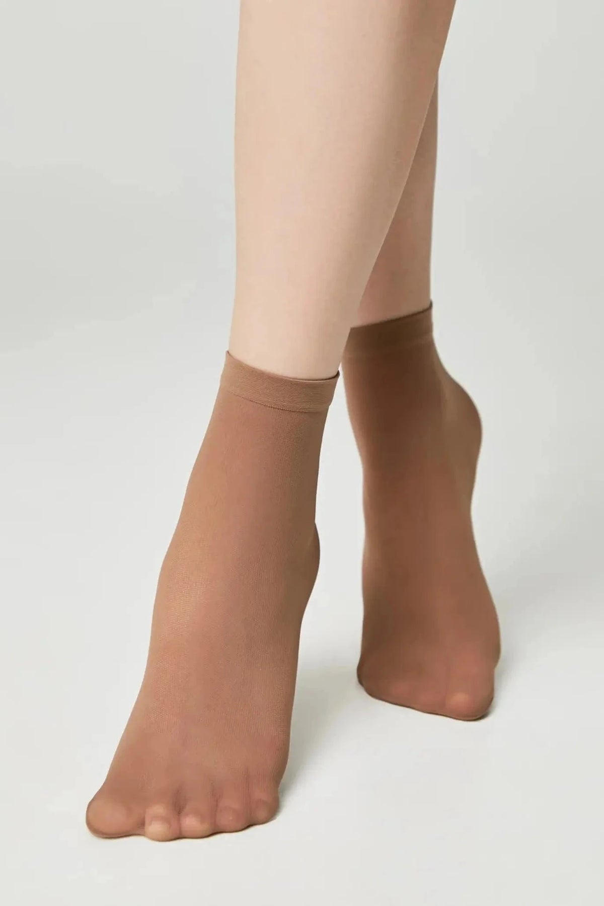 A pair of sheer, nude-colored ankle socks worn on a person's feet against a plain light background.