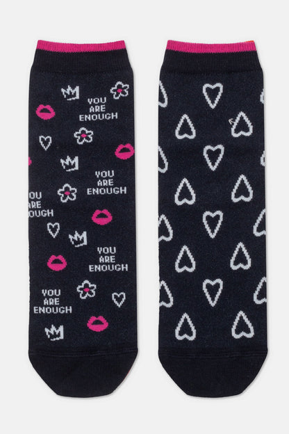 A pair of black ankle socks featuring a print of white hearts, pink lips, crowns, flowers, and the phrase "YOU ARE ENOUGH" in white text, with pink cuffs at the top.