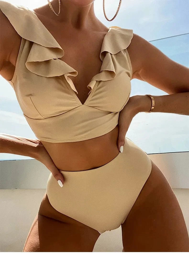 A beige two-piece swimsuit with a ruffled V-neck crop top and a high-waisted bottom worn by a person outdoors.