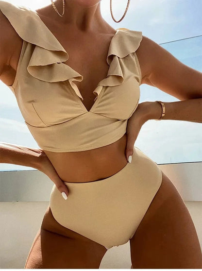 A beige two-piece swimsuit with a ruffled V-neck crop top and a high-waisted bottom worn by a person outdoors.