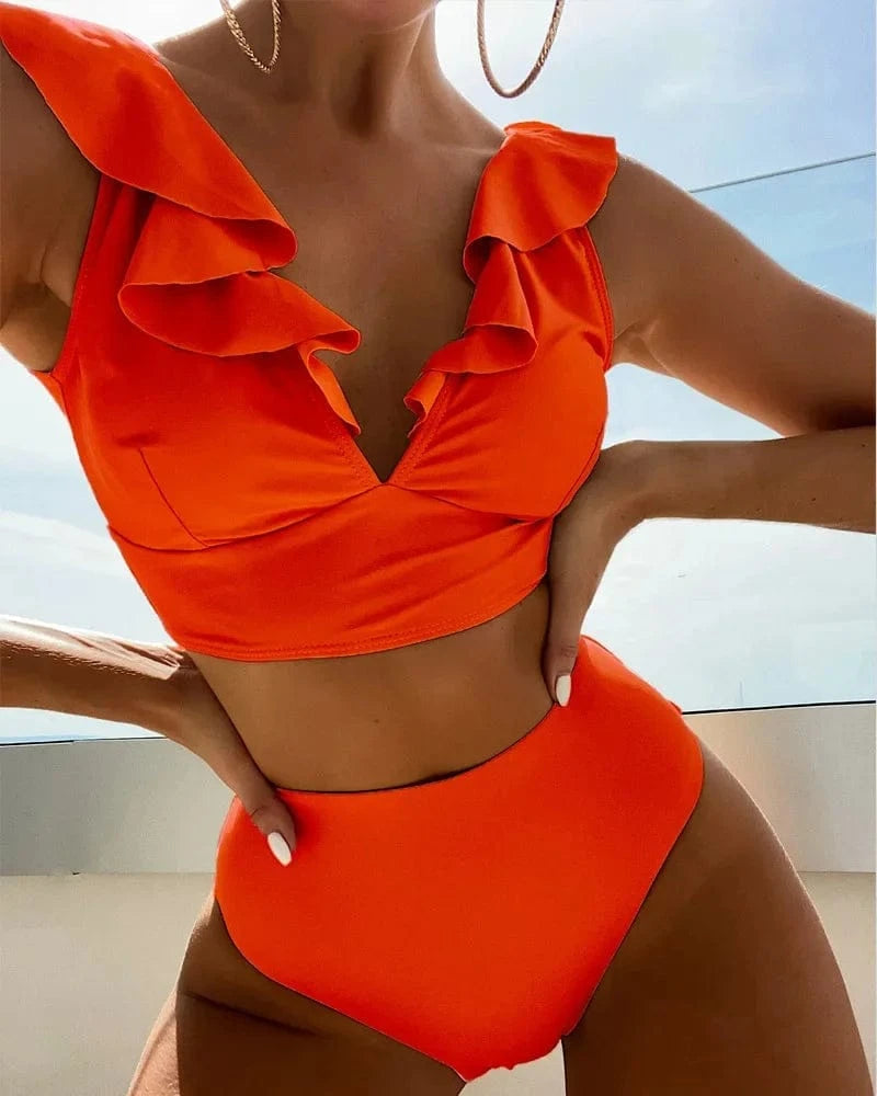 A woman wears a bright orange two-piece bikini featuring a ruffled V-neck crop top and high-waisted bottoms.