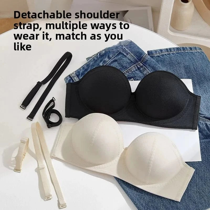 Two strapless bras, one in black and one in beige, lie on a white surface next to a pair of blue denim jeans and their corresponding detachable shoulder straps.