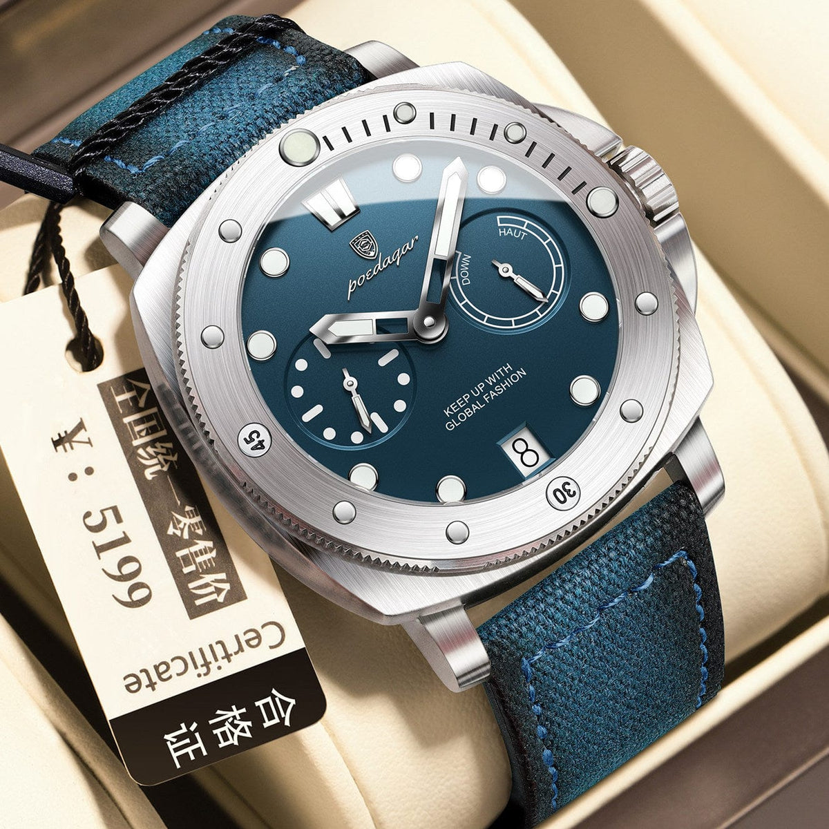 A round stainless steel wristwatch with a blue dial, luminous markers, two subdials, a date window, and a dark blue textured strap, displayed next to a rectangular certificate tag.
