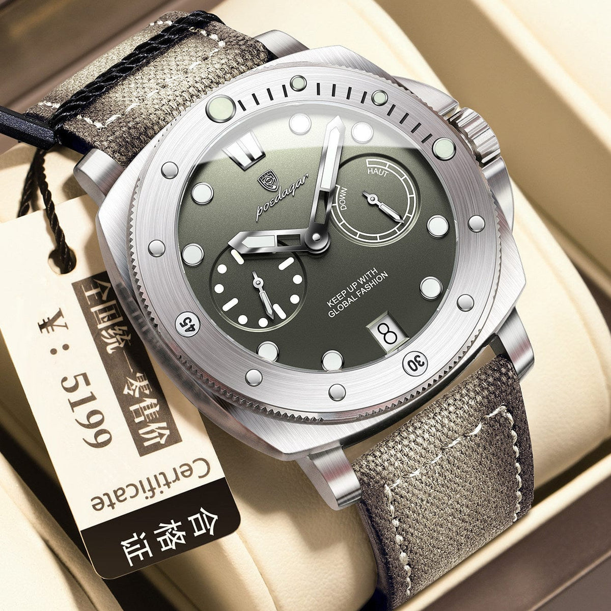 A round stainless steel watch with a gray face, luminous markers, two sub-dials, and a date display, secured to a gray fabric strap and resting on a beige cushion next to a product certificate tag.