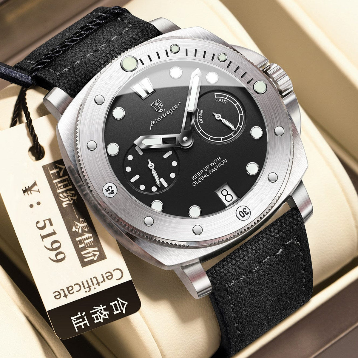 A men's wristwatch with a round black dial featuring two subdials, a date display, and a brushed silver bezel set against a black fabric strap inside a gift box.