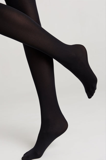 Opaque black tights worn on a person with legs crossed against a plain light gray background.