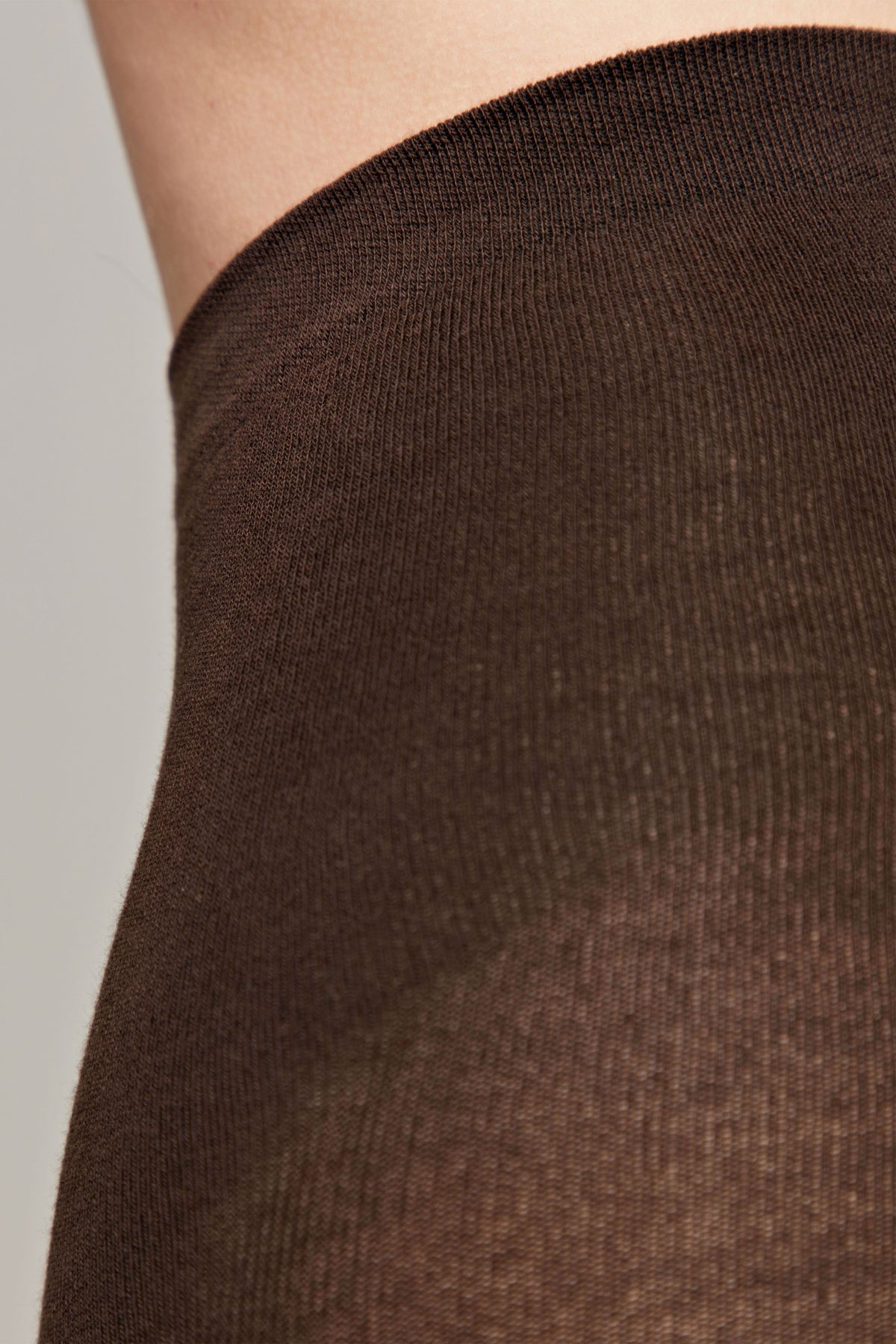 A close-up view of dark brown knit fabric worn against skin, showcasing the fine texture and weave of the material.