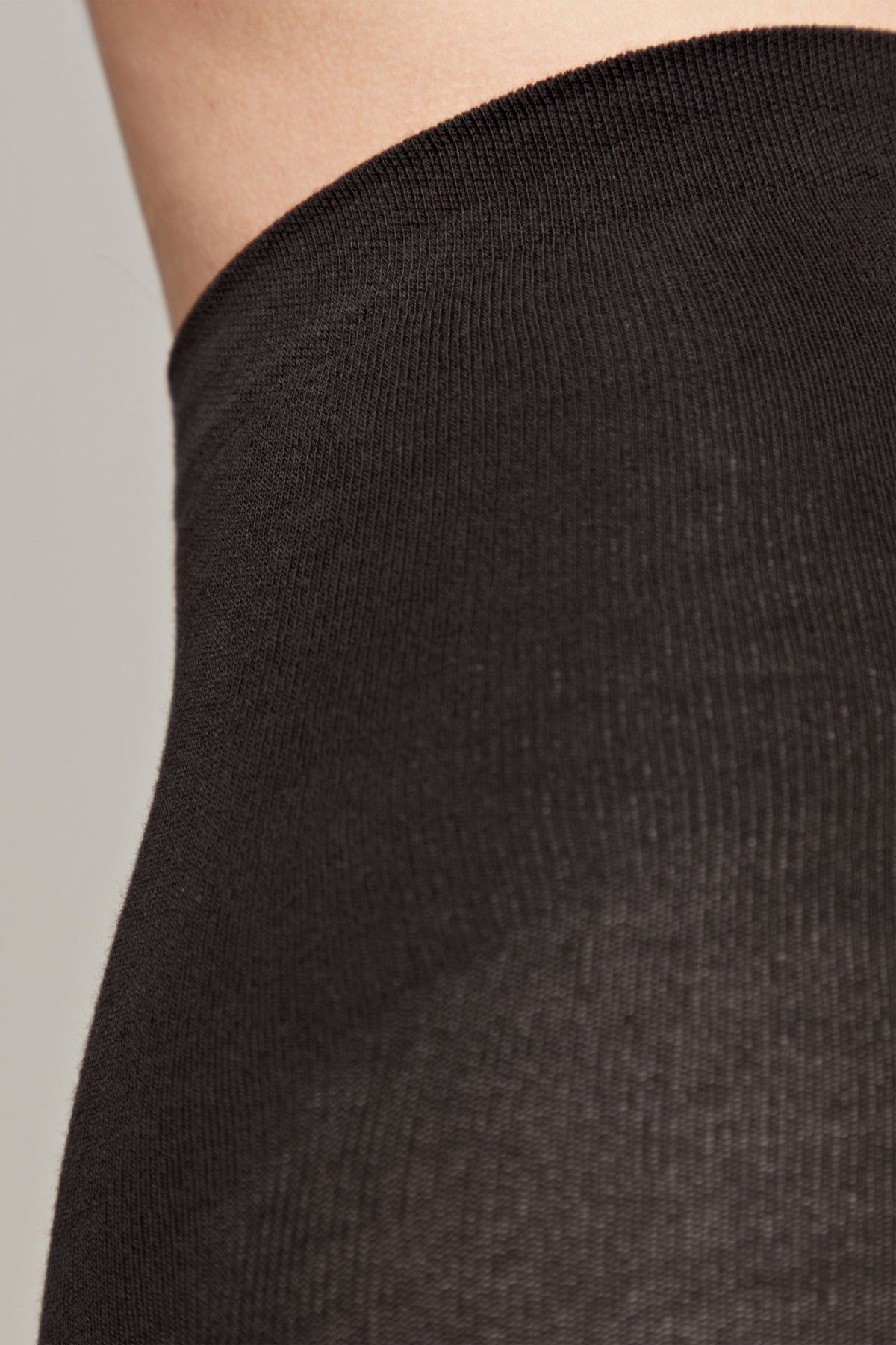 A close-up of a black fabric garment worn against skin, showcasing the fine knit texture and the straight edge of the cuff.