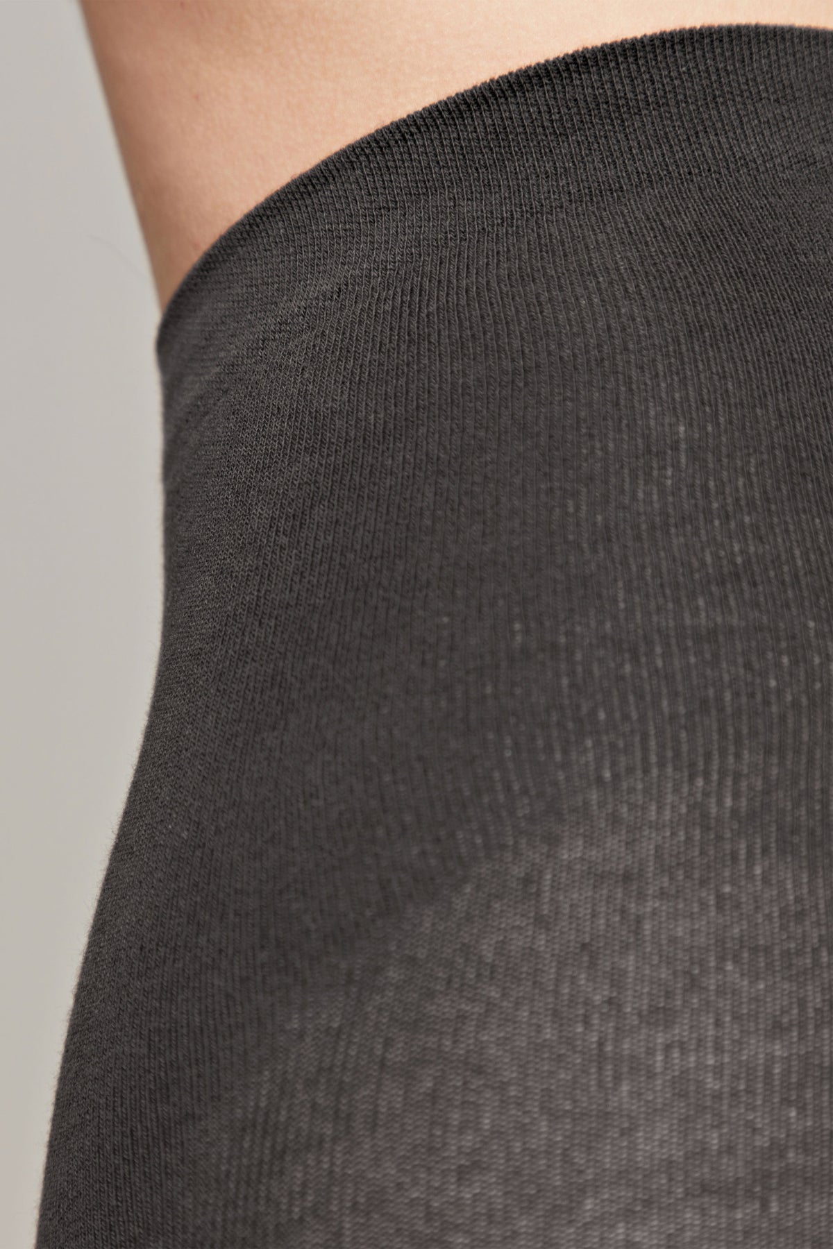 A close-up view of the charcoal grey fabric of a pair of socks worn on an ankle.