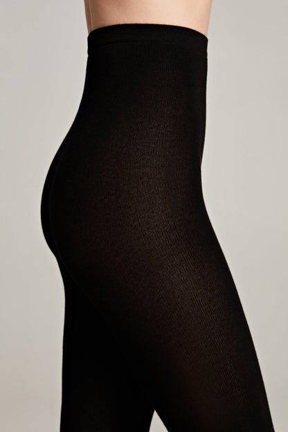 Black tights worn by a person, showing a high-waisted fit and a close-up profile view of the hips and legs against a neutral background.