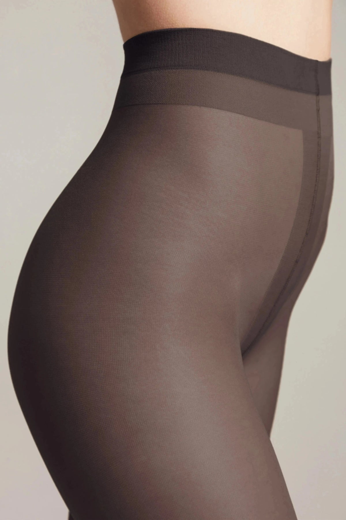 A close-up side view of a person wearing sheer, dark brown pantyhose against a plain, light background.