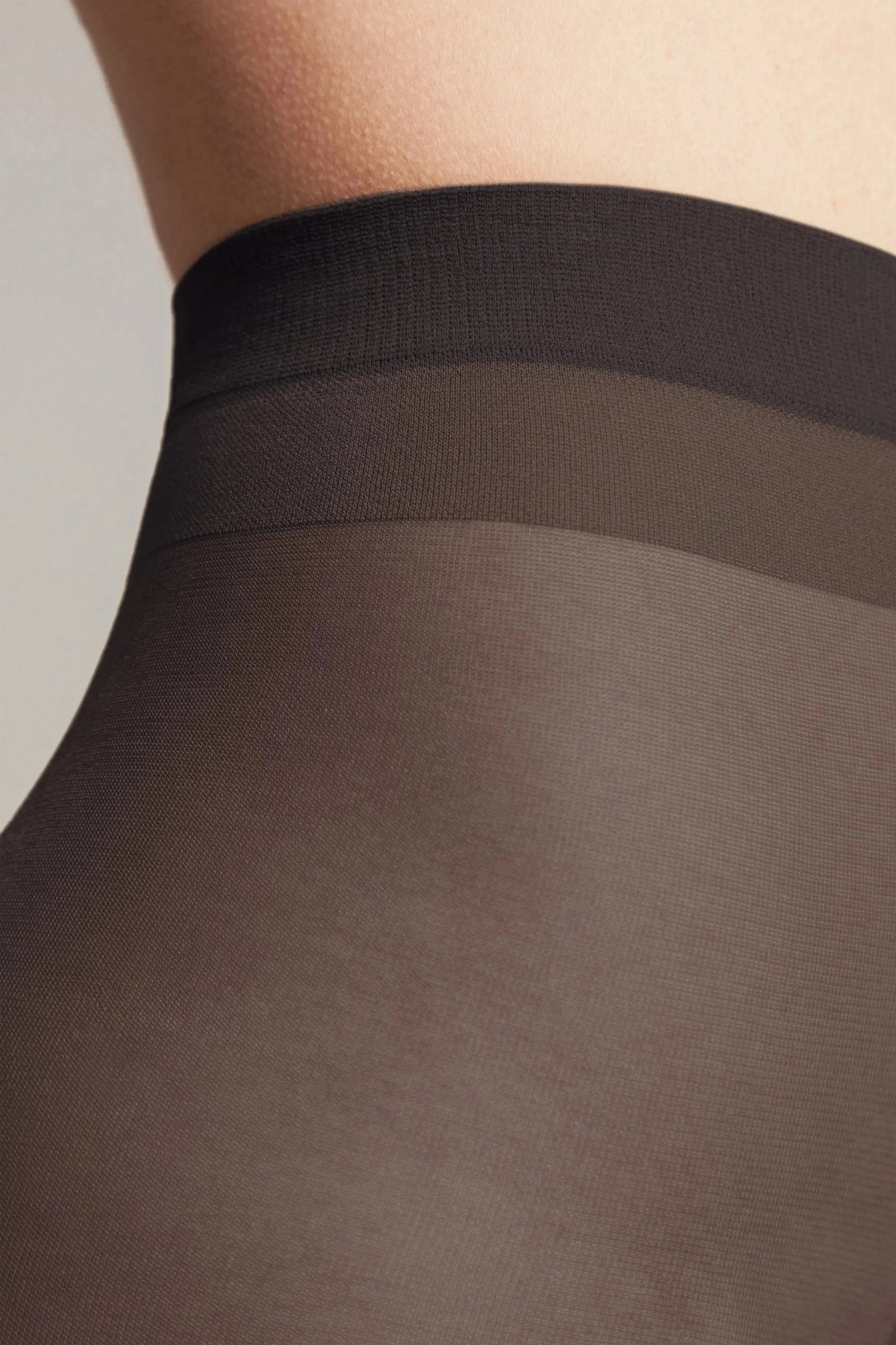 A close-up view of black sheer hosiery worn on a person's torso, featuring a darker, reinforced waistband.