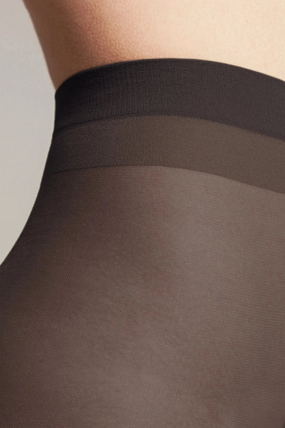 A close-up view of black sheer hosiery worn on a person's torso, featuring a darker, reinforced waistband.