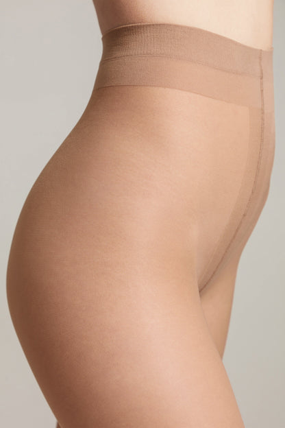 A close-up side view of nude-colored pantyhose on a person's lower torso and upper thigh against a plain light gray background.