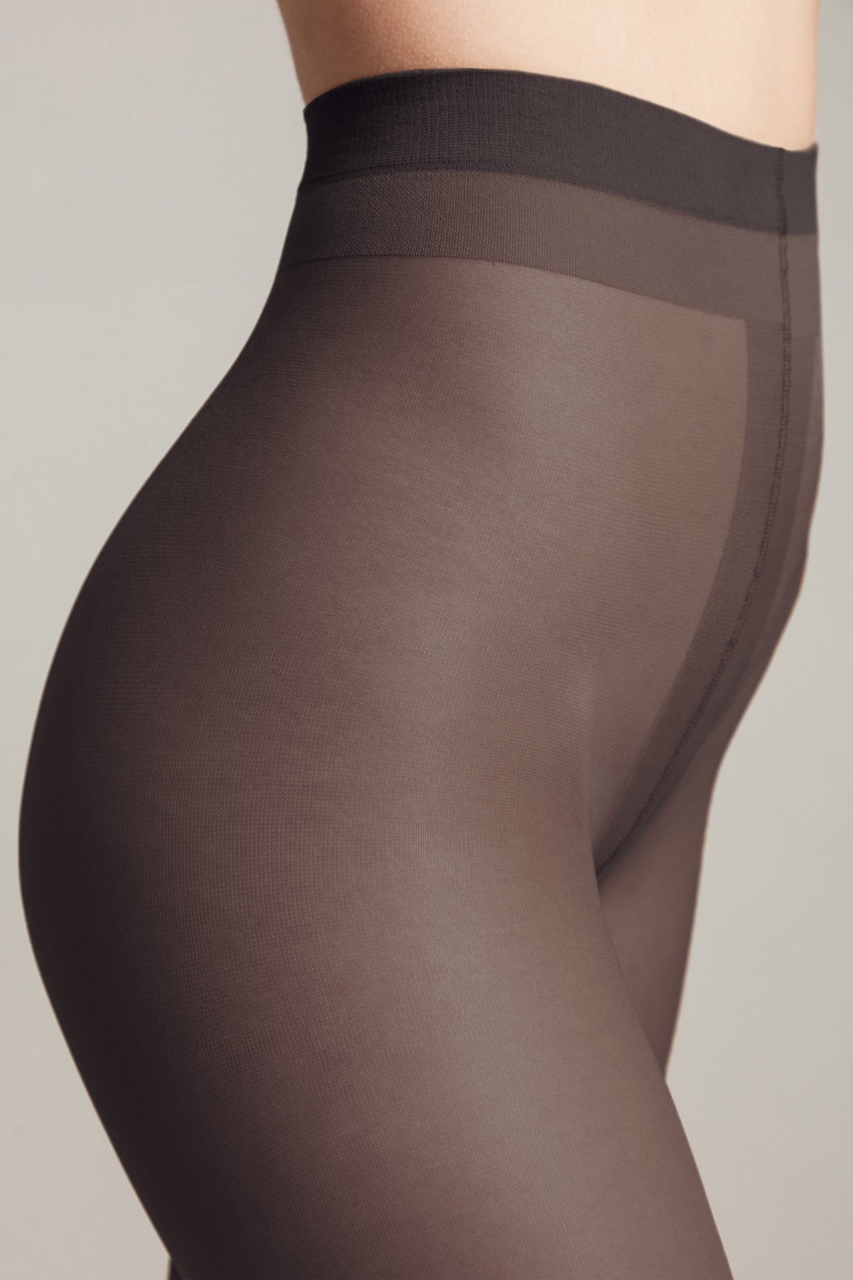 A close-up view of dark brown sheer tights worn on a person's hips and upper thighs against a plain grey background.