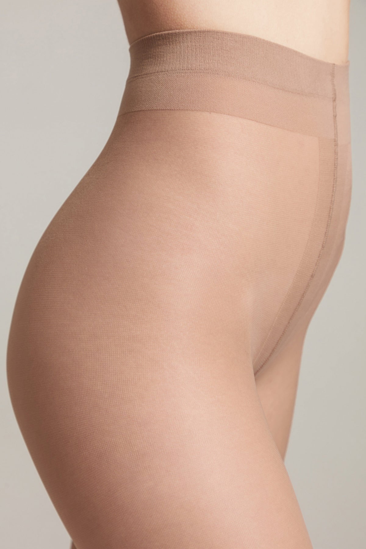 A close-up side profile view of sheer beige pantyhose worn on a person, featuring a high-waisted design with a reinforced waistband against a neutral background.