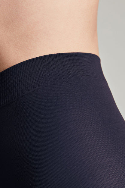 A close-up view of navy blue tights featuring a thick, elasticated waistband against a person's torso.