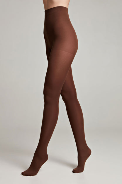 A person wearing opaque dark brown tights against a plain grey background.