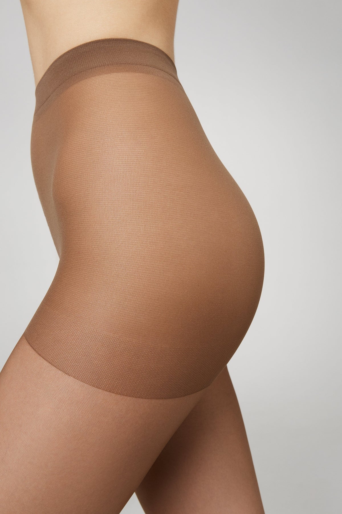 A pair of sheer tan-colored pantyhose worn on a person, featuring a reinforced control-top waistband.