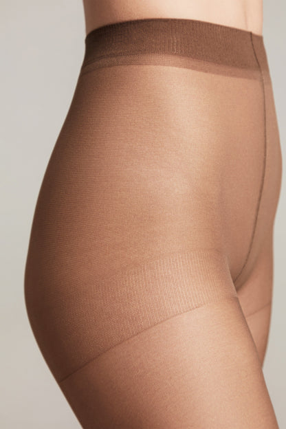 A close-up side view of a person wearing sheer tan pantyhose with a darker brown waistband against a neutral background.