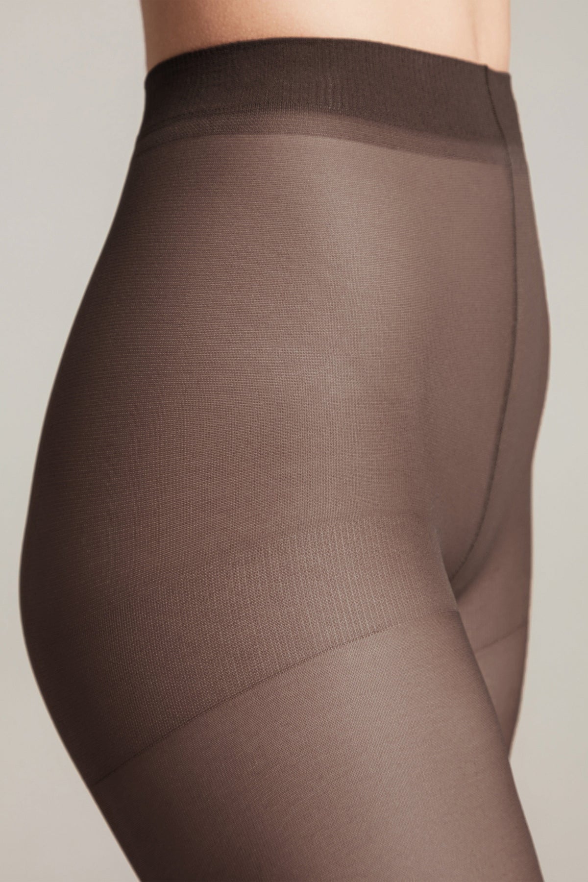 Sheer dark brown tights worn on a person, featuring a high-waisted waistband and a reinforced panty section.