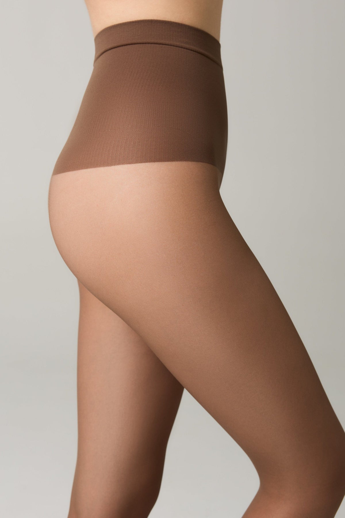 A close-up side profile view of a person wearing sheer tan tights with a seamless high-waist band on a plain light grey background.