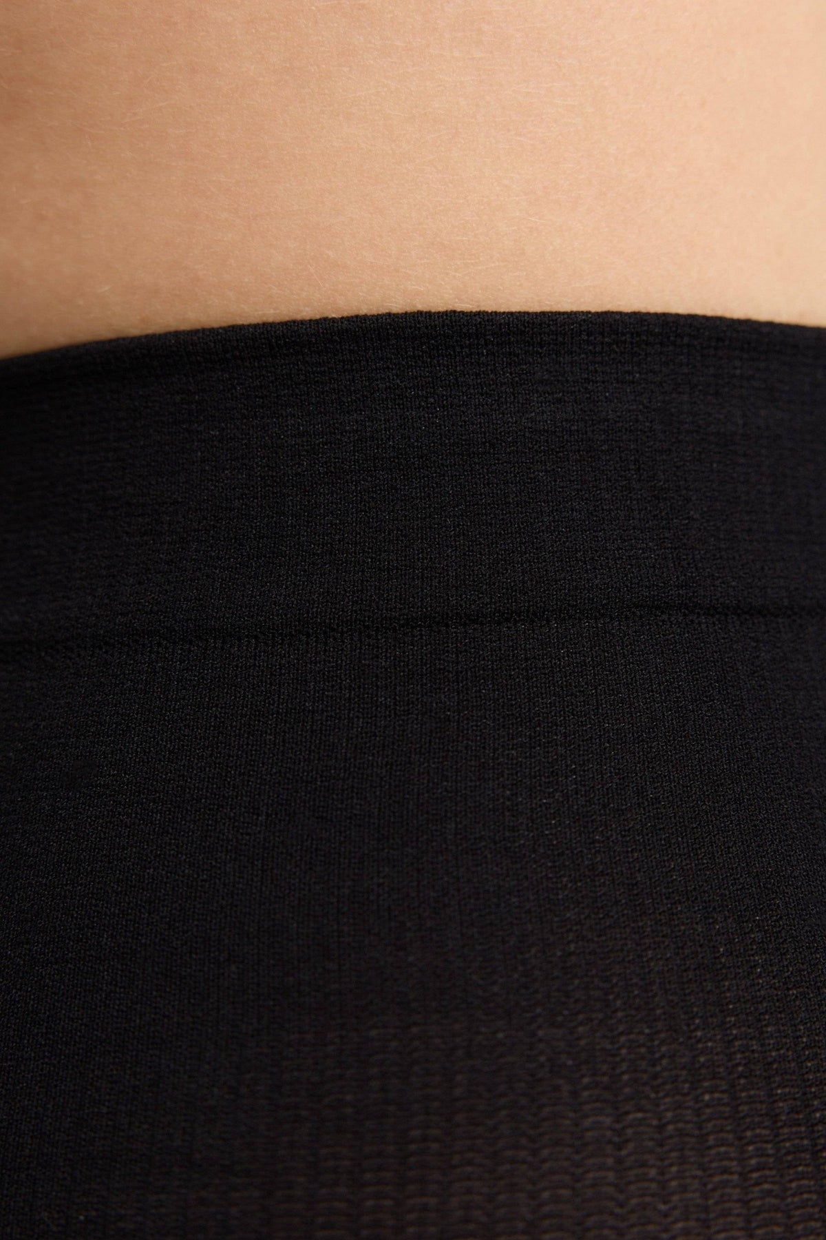 A close-up view of a black knit waistband resting against a person's skin.